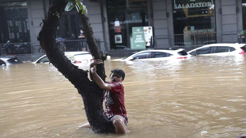 A man grabs a tree to keep from being swept away by flood water through a flooded neighborhood following heavy rains in Jakarta, Indonesia.